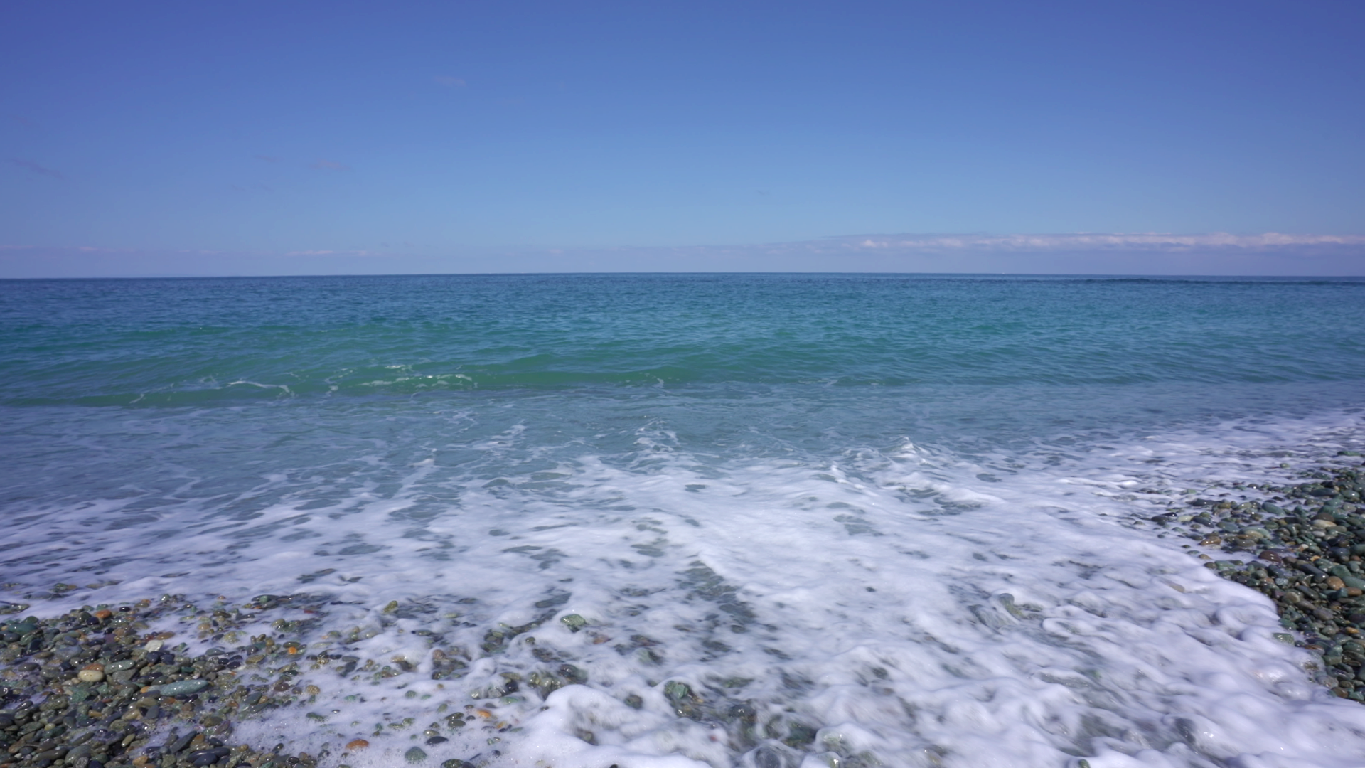 青い海と波が打ち寄せる石浜。自然のリズムを感じる情景